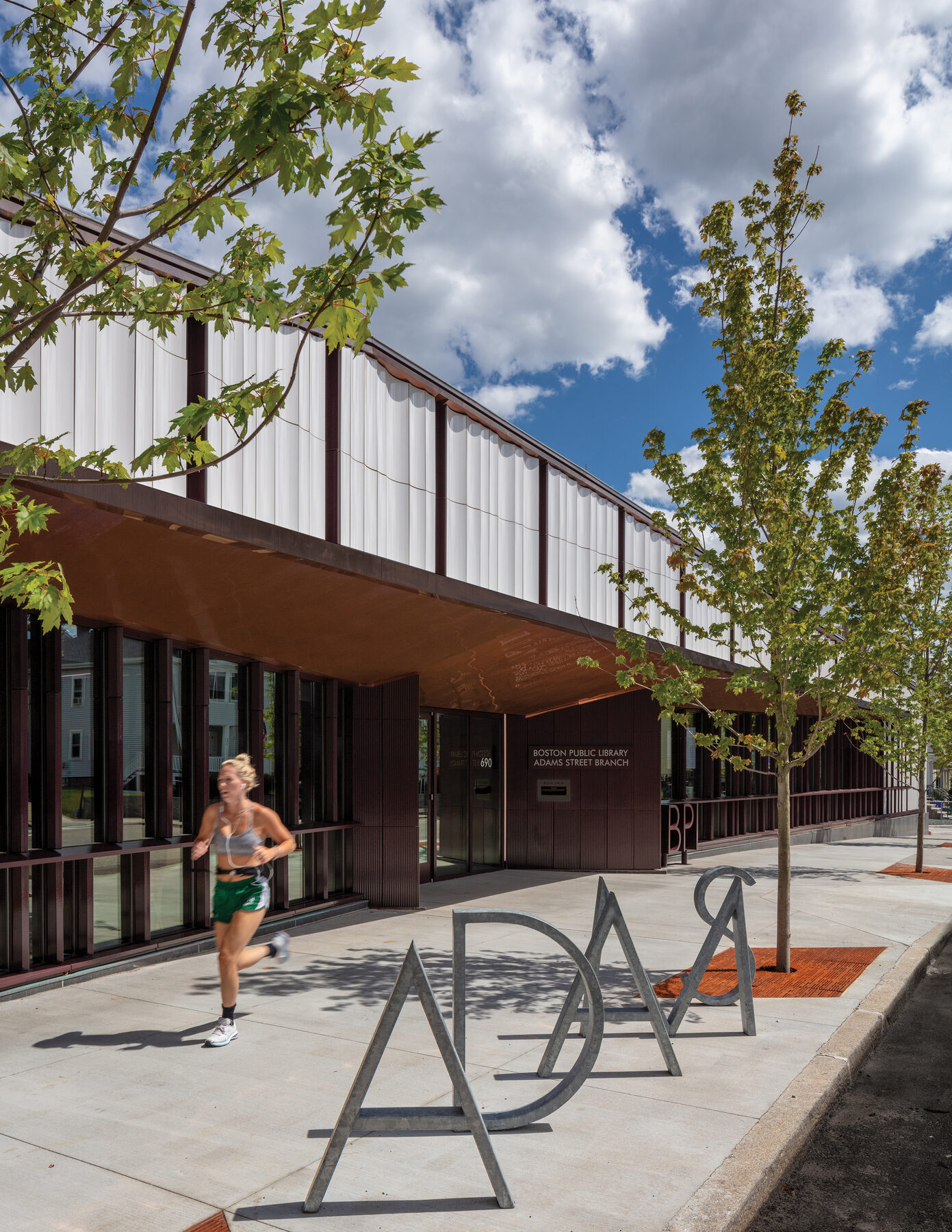 Adams Street face by day, with the library's ADAMS sculpture in the foreground and a runner passing