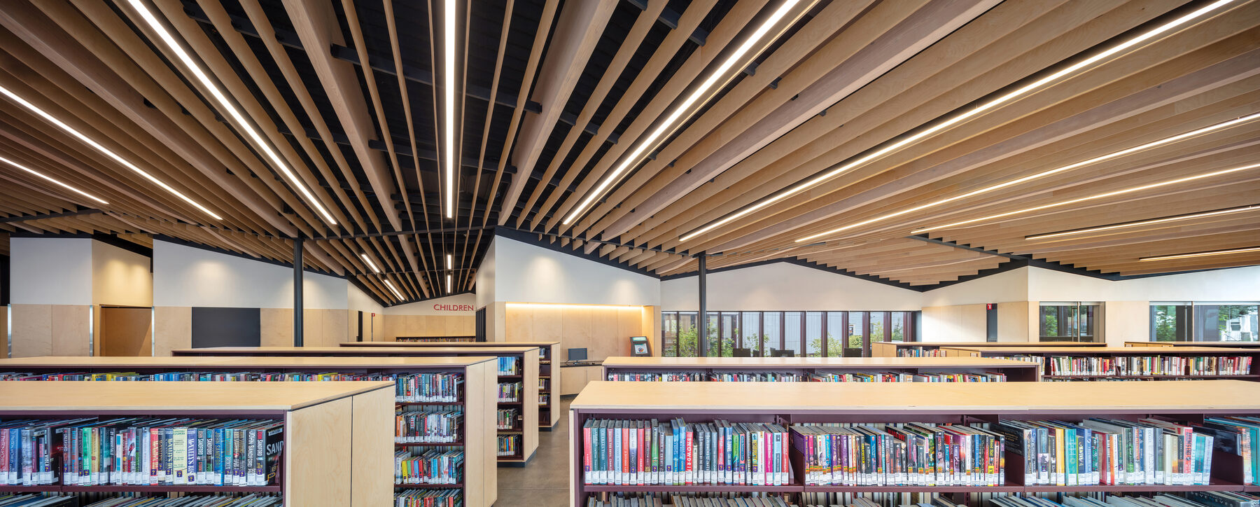 Wide interior view showing the rolling plywood fins overhead and the central circulation desk with the children's wing beyond