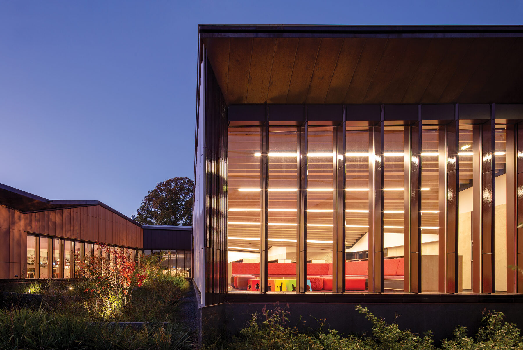 The rear of the library at twilight, with two of the smaller-scale gable volumes glowing through the garden