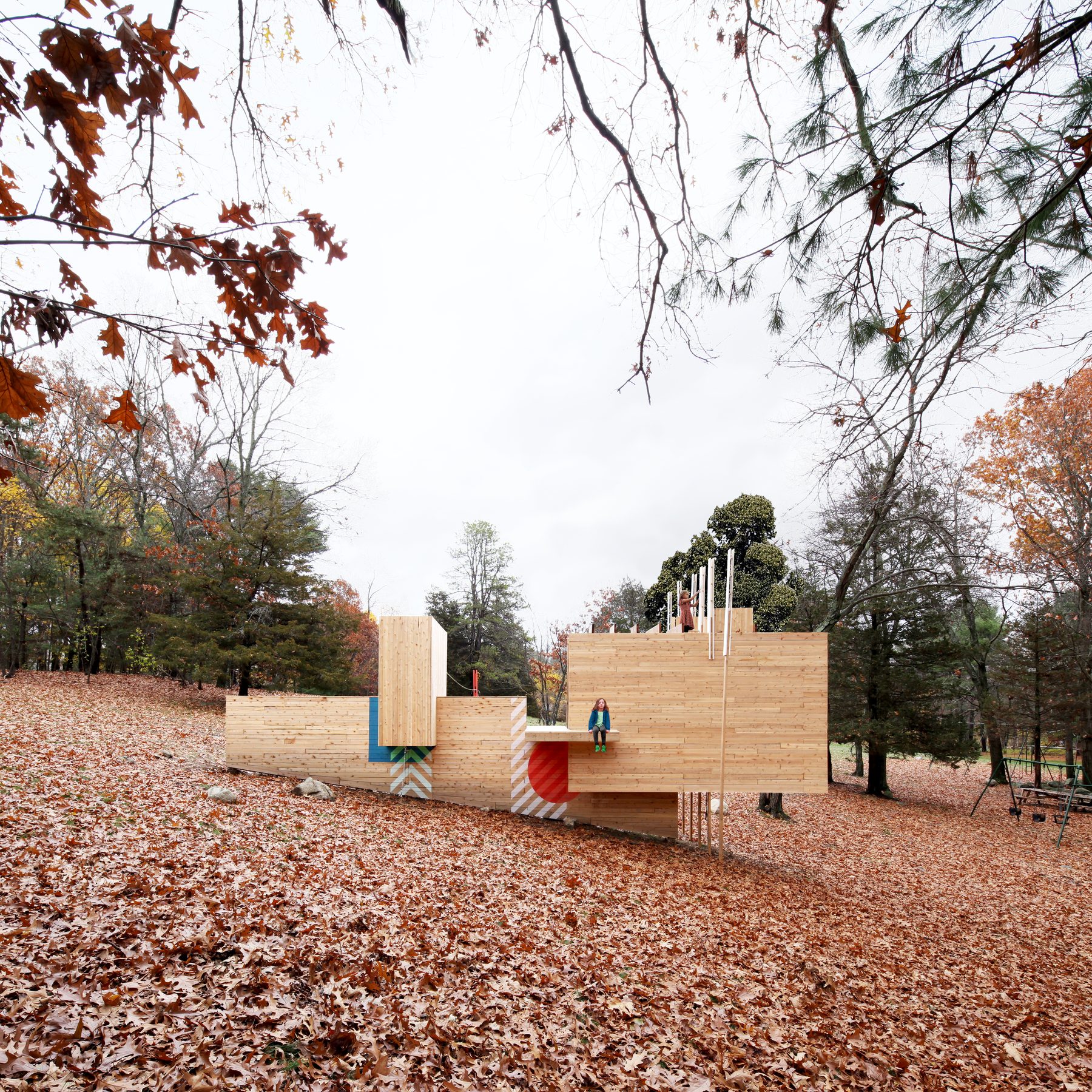 The structure framed by an oak branch at the upper left, two children playing &mdash; one seated on a cantilevered shelf, one on top