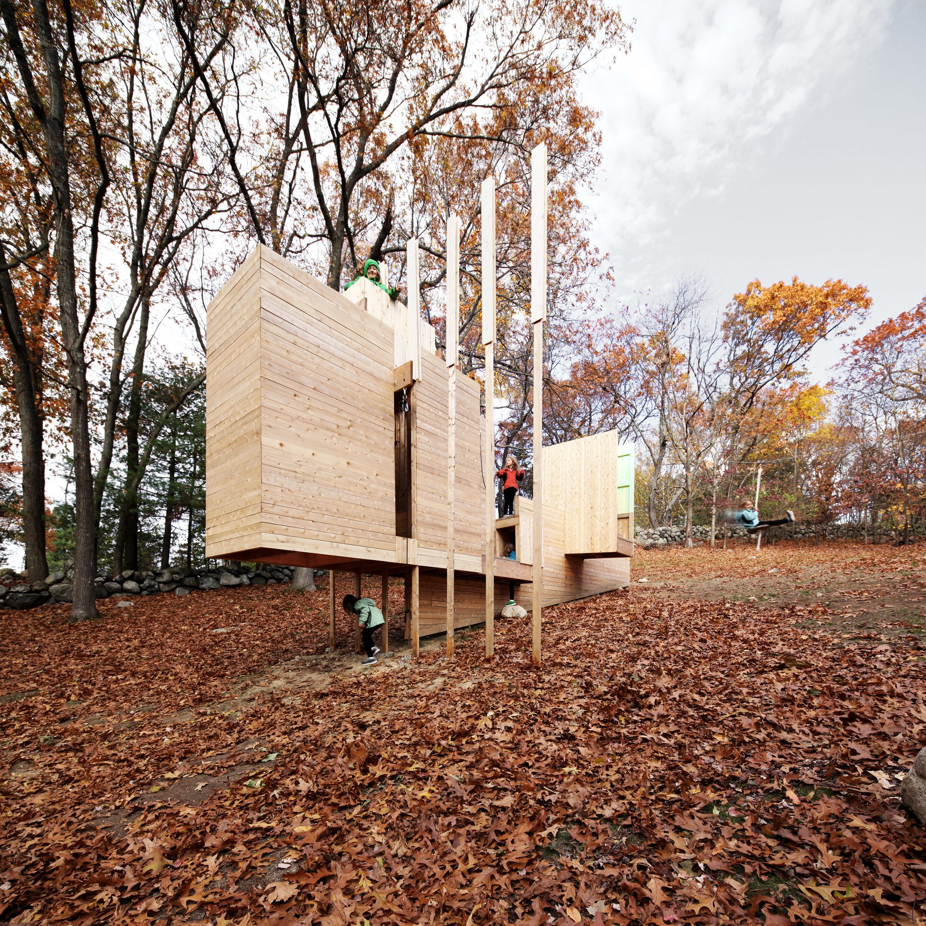 The structure being used &mdash; one child on top, one descending stairs, one climbing in from below, and one in motion on the zip-line at the right edge