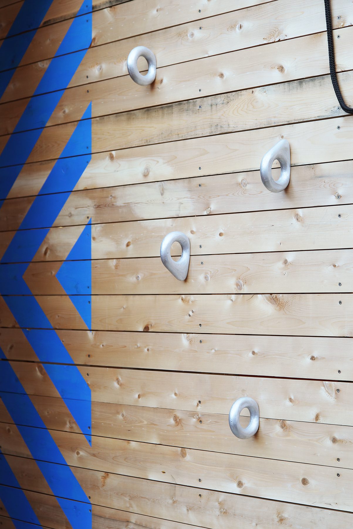 Cast aluminum climbing holds set in the wood wall alongside a painted blue chevron graphic