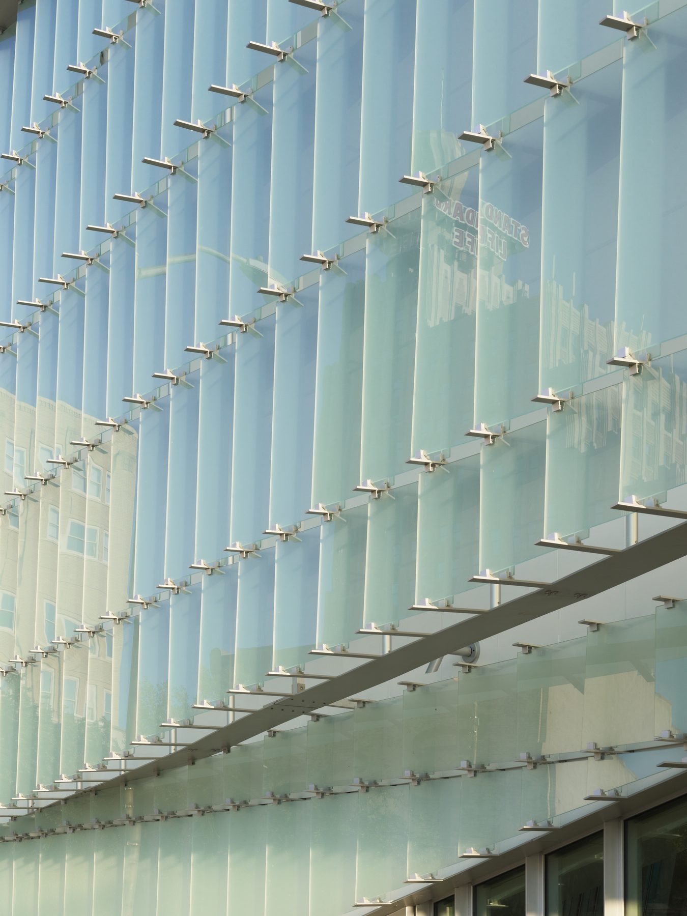 Looking up at the glass-shingle skin, the aluminum rails growing longer as they rise