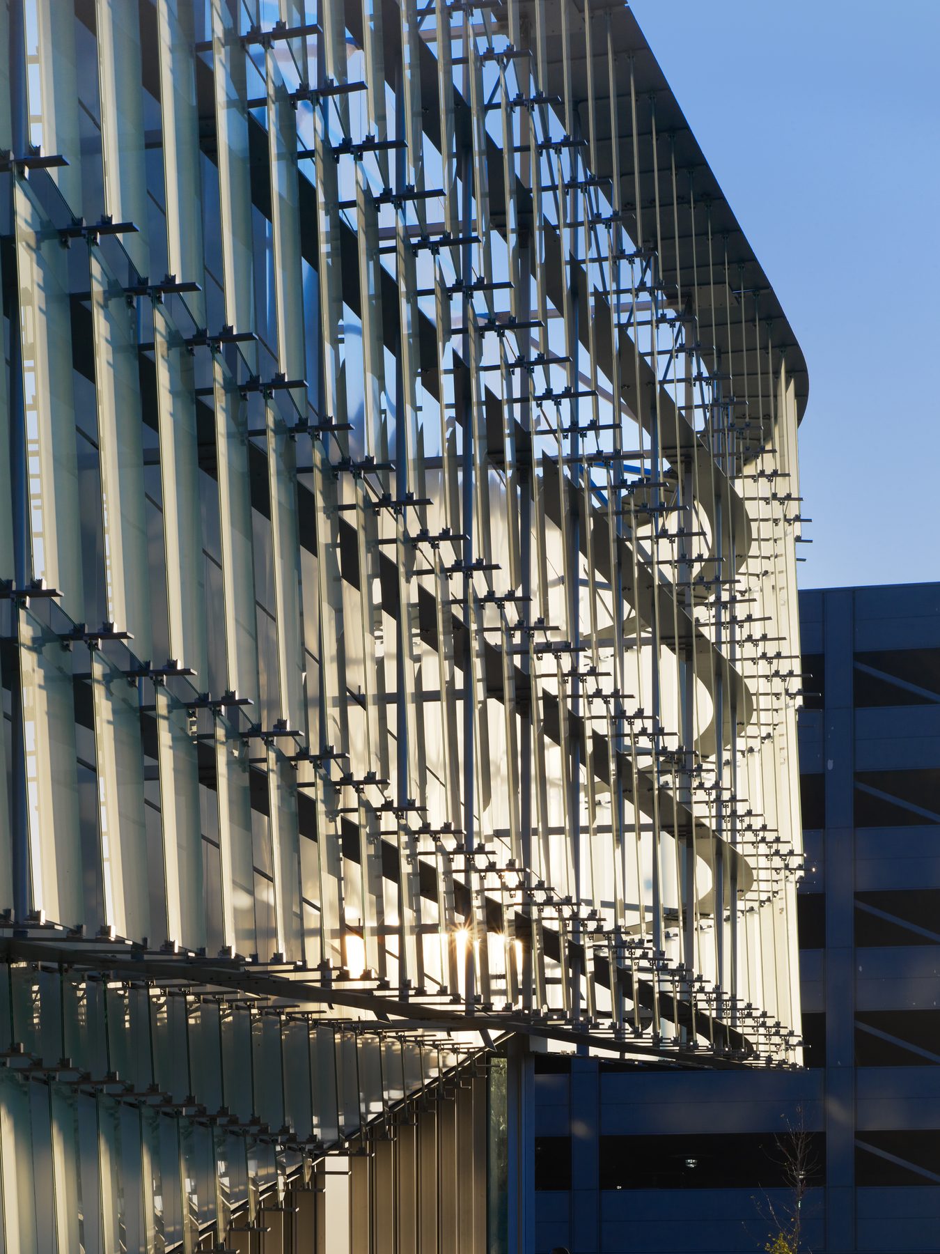 The ribbon-and-quill structure backlit at dusk, the aluminum rails reading as a vertical rhythm