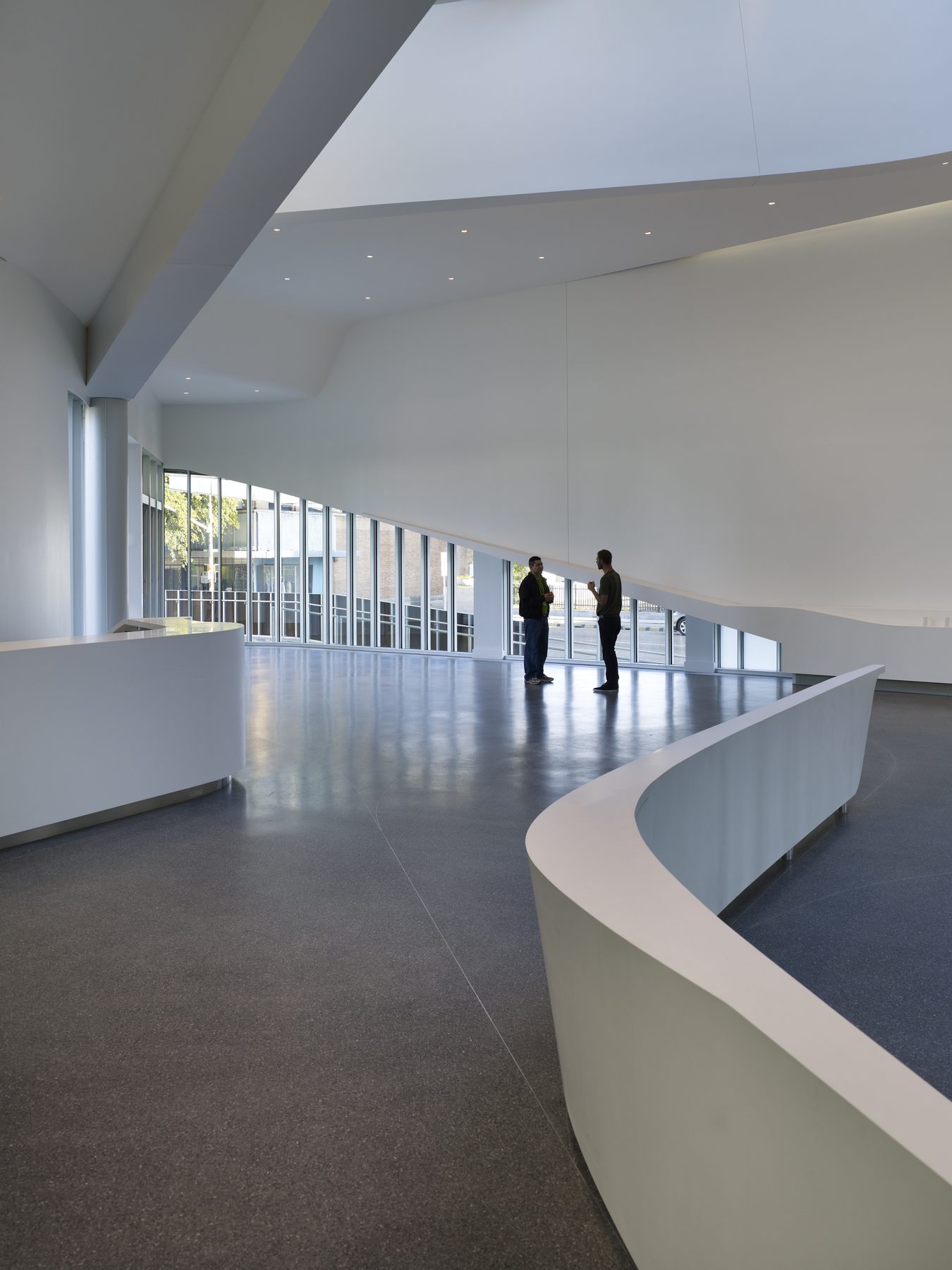 The curved white counter and full-height glazing at the lobby, two people in conversation beside the windows