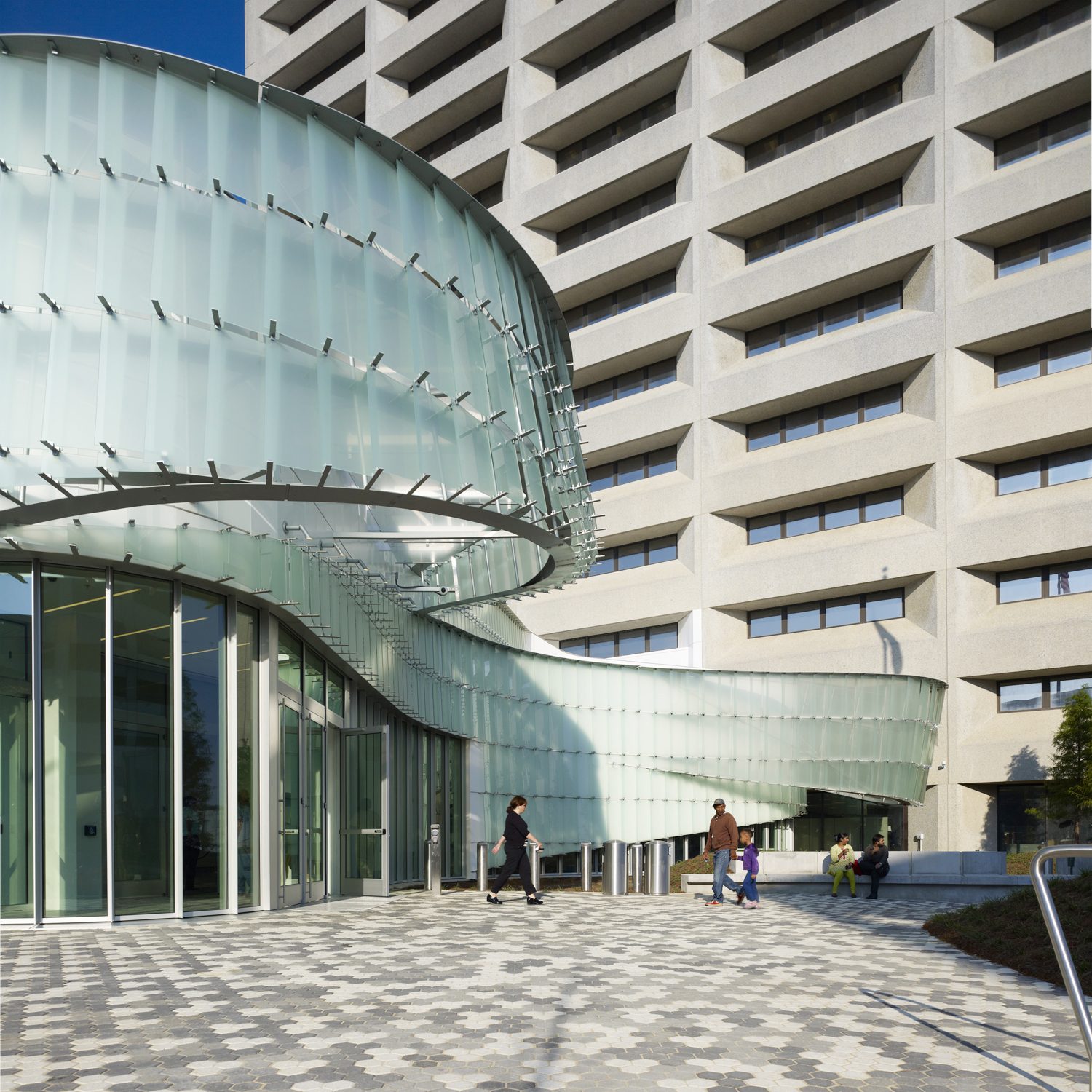 The McCoy pavilion's translucent glass-shingle curve against the concrete grid of the federal tower behind it